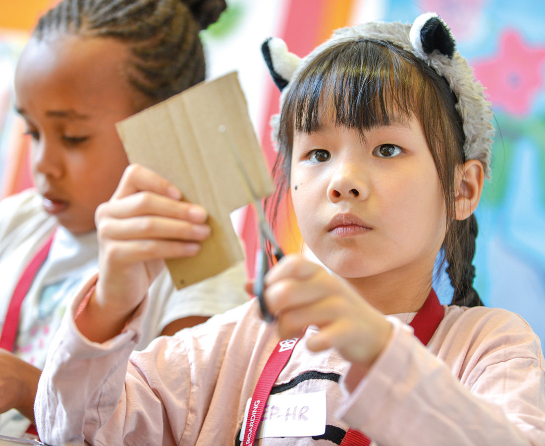 Female student cutting carboard for a craft activity at camp dragon